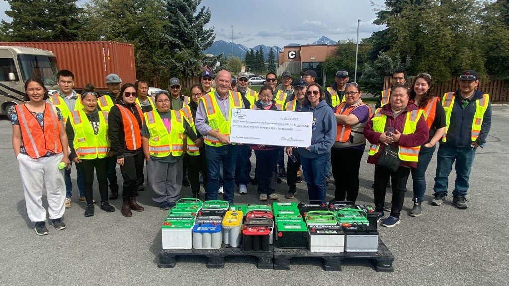 A group of people accept a cheque in Alaska in front of some used lead acid batteries