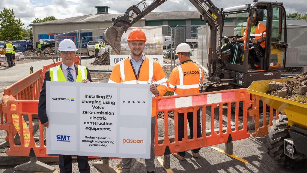 Two workers hold a sign on a job site utilizing electric equipment