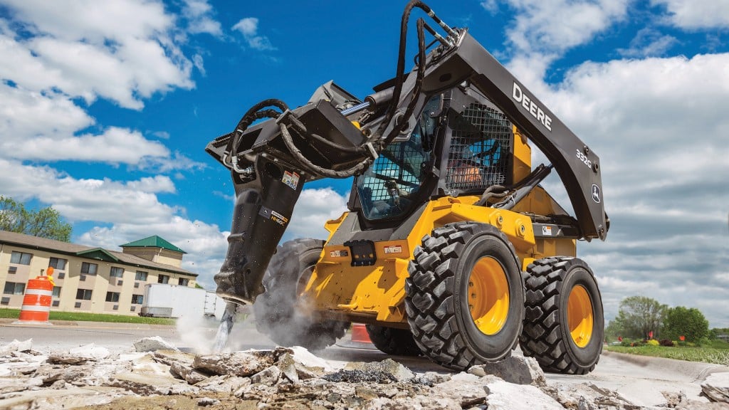 A skid-steer loader uses a breaker on a job site