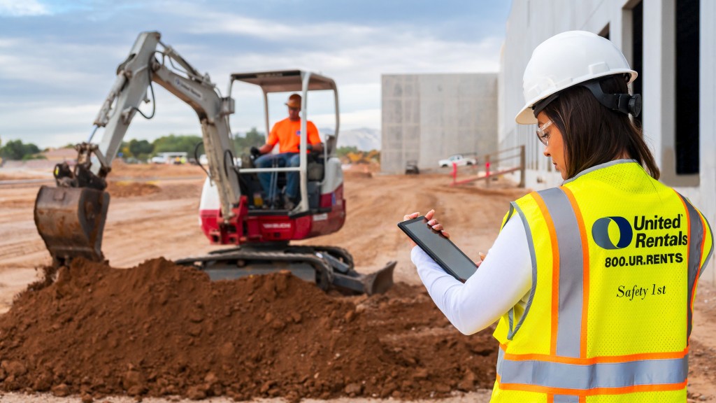 An operator uses a mini excavator and another uses a tablet on a job site