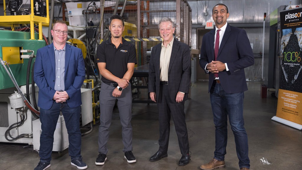 Four people pose for a photo inside of a recycling facility