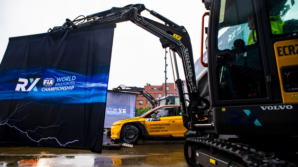 Excavators hold up fabric signs around a racecar