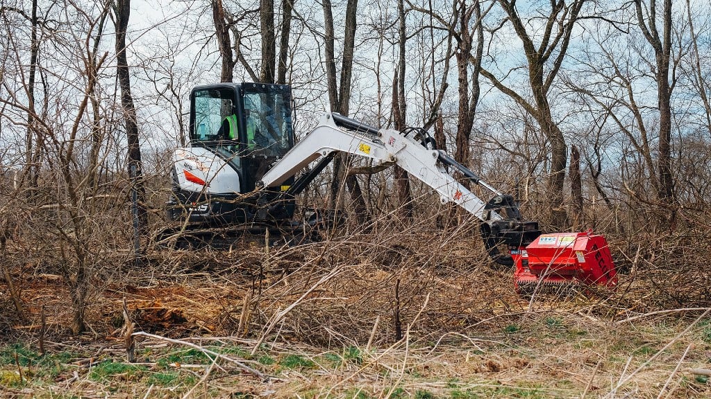 A compact excavator uses a mulcher attachment on a job site