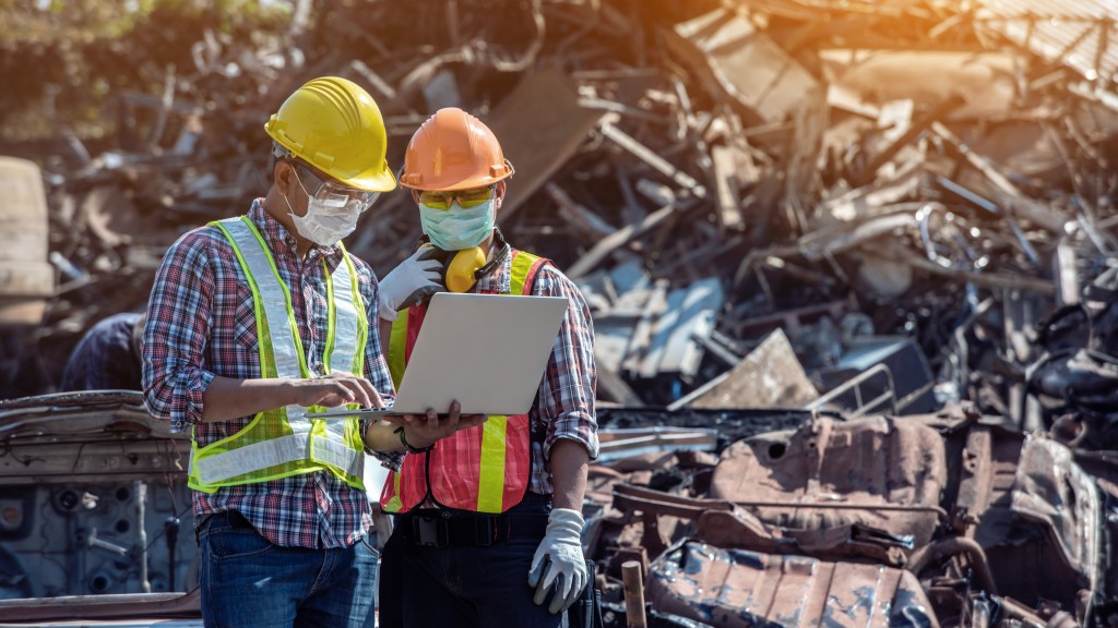 Two people use a laptop at an automotie recycling yard