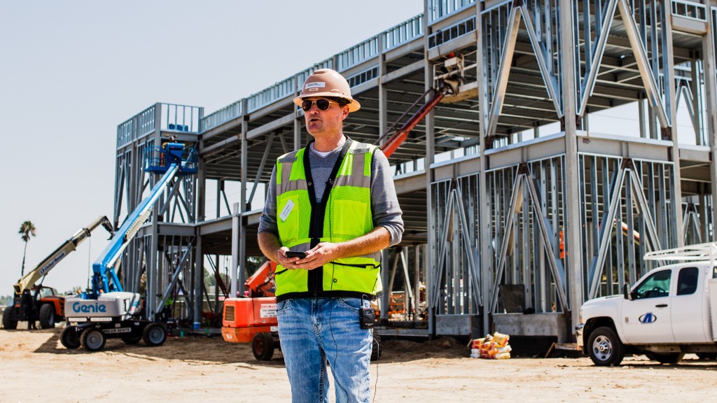 A worker in hi-vis holding a phone in front of a building site