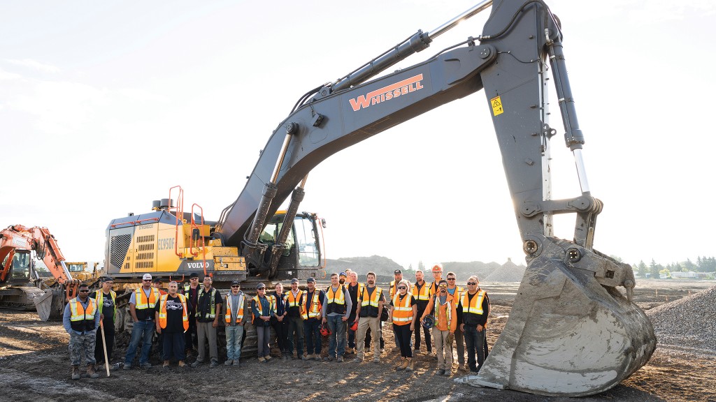 A group of people pose for a photo around an excavator