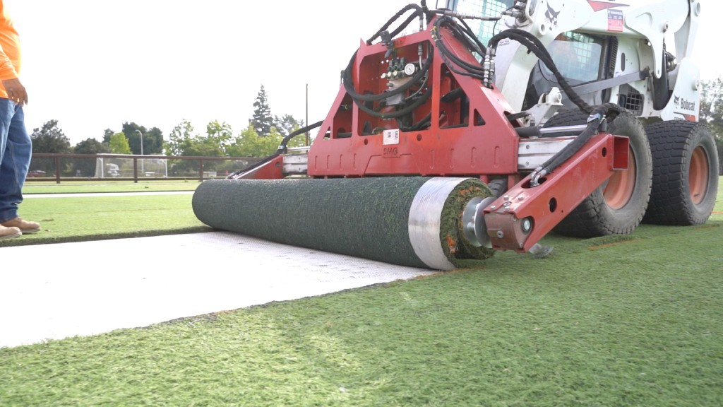 A skid-steer loader lays turf on a synthetic field