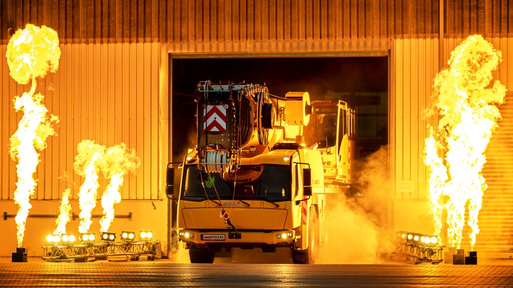 An all-terrain crane drives through an open door surrounded by flames