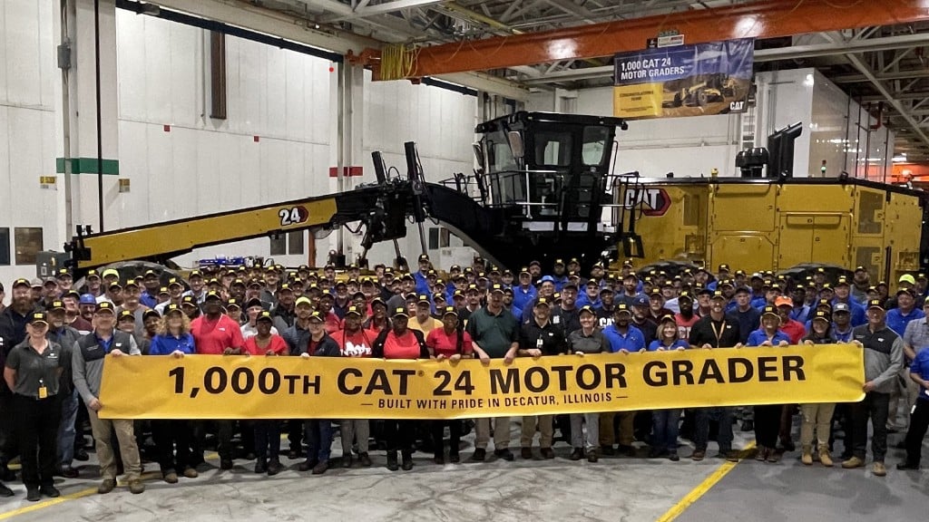 A group of people stand in front of a motor grader