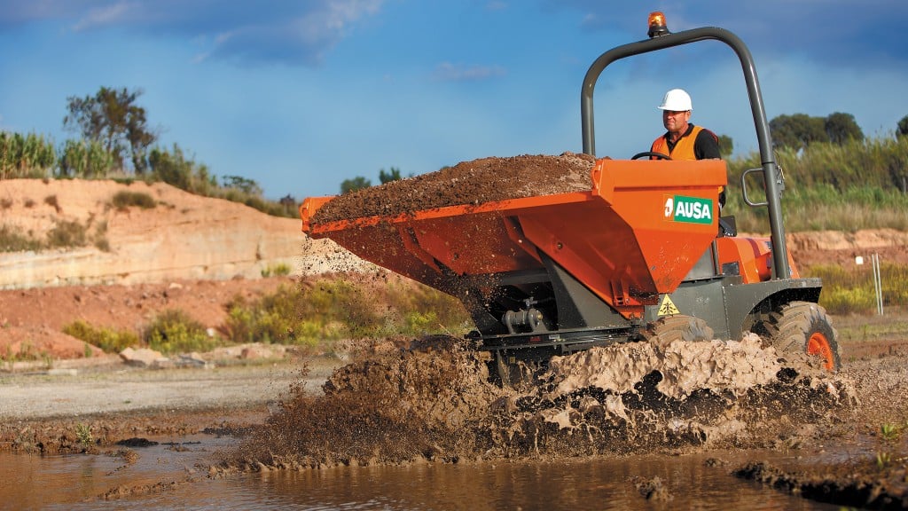 A site dumper with a bucket full of dirt drives through a muddy puddle
