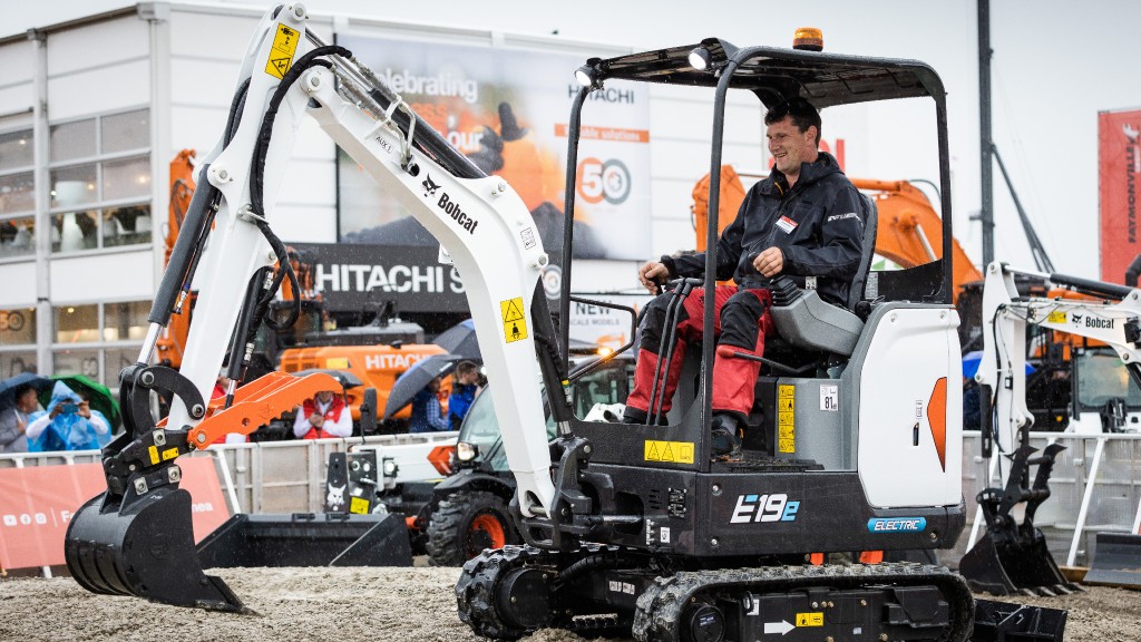 A worker operates a compact excavator in a demo area