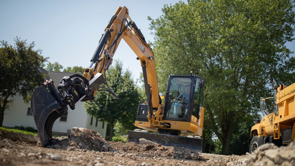 An excavator using a tilt rotate system digs a hole on a job site