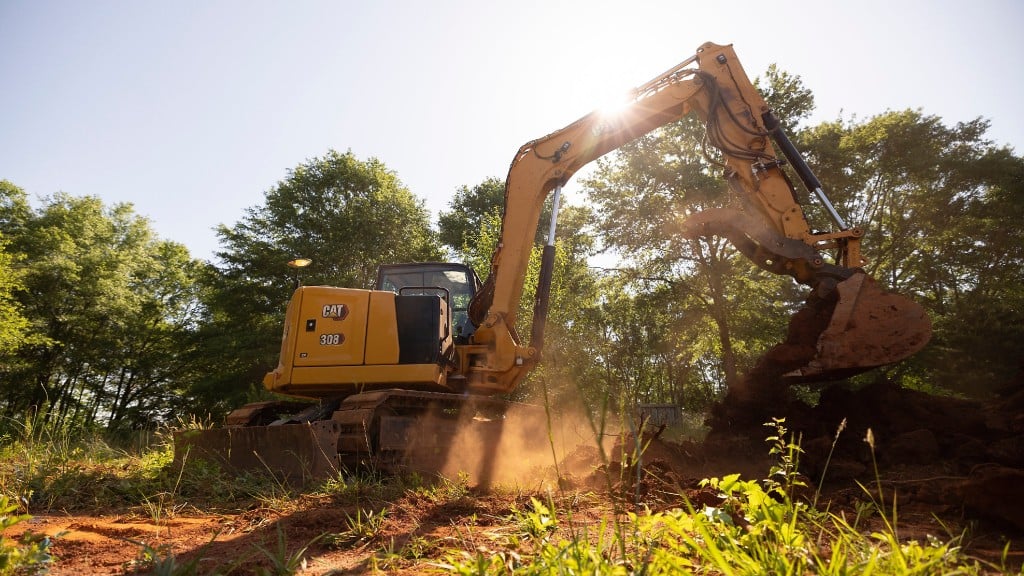 A mini excavator digging dirt silhouetted against the sun