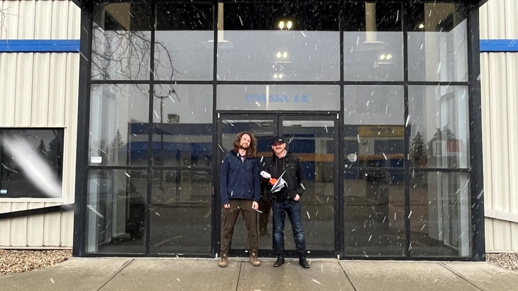 Two men stand in front of an empty storefront in the snow