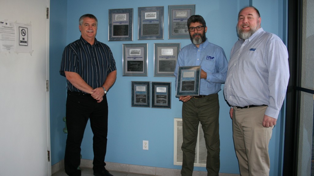 Three people pose for a photo with an award