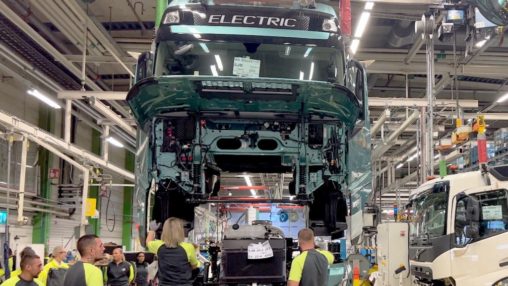 Factory workers surround an electric truck on a hoist