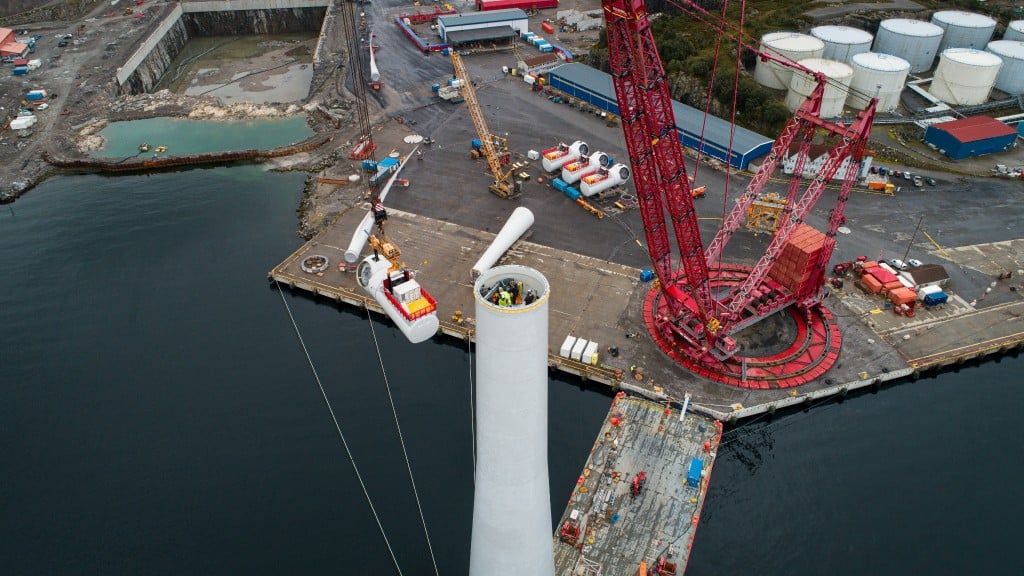 Aerial view of cranes on a shoreline assembling a wind turbine