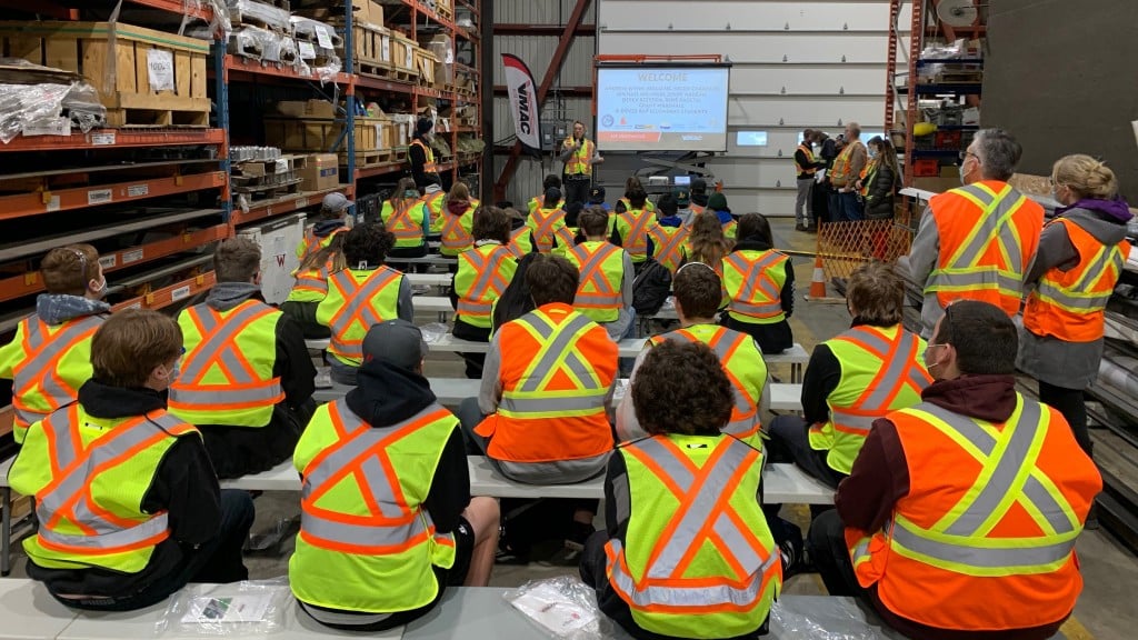 Students sit and watch a powerpoint in a manufacturing facility