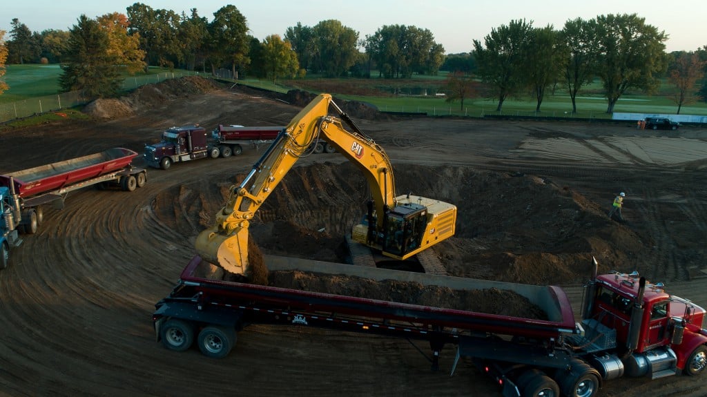 An excavator in a round digging site loading semi trailer trucks