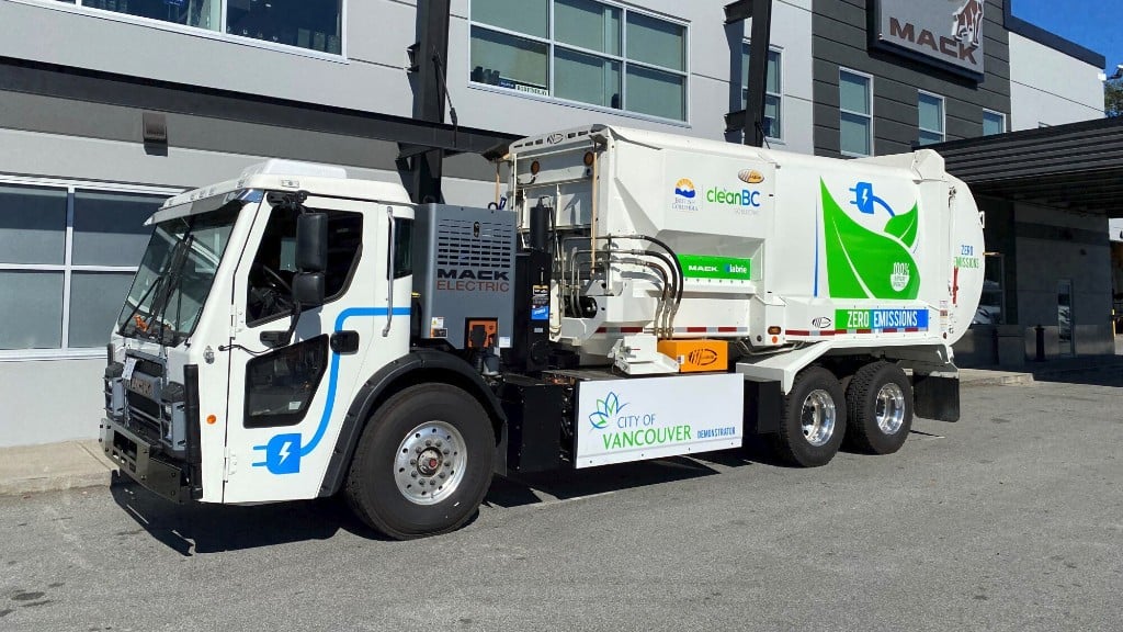 An electric collection truck is parked near a building