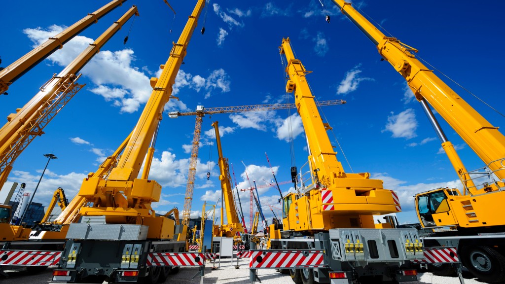 A number of cranes with their booms raised against a blue sky with wispy white clouds