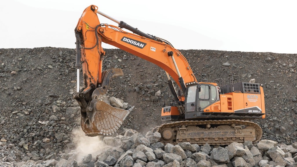 An excavator lifts up a bucket full of rocks
