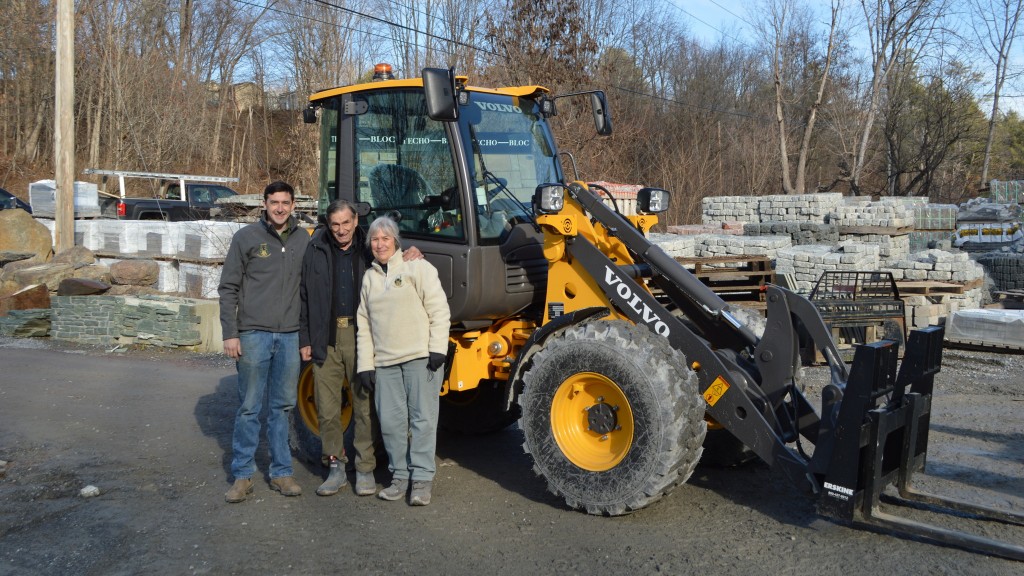 Three people pose for a photo near an electric compact wheel loader