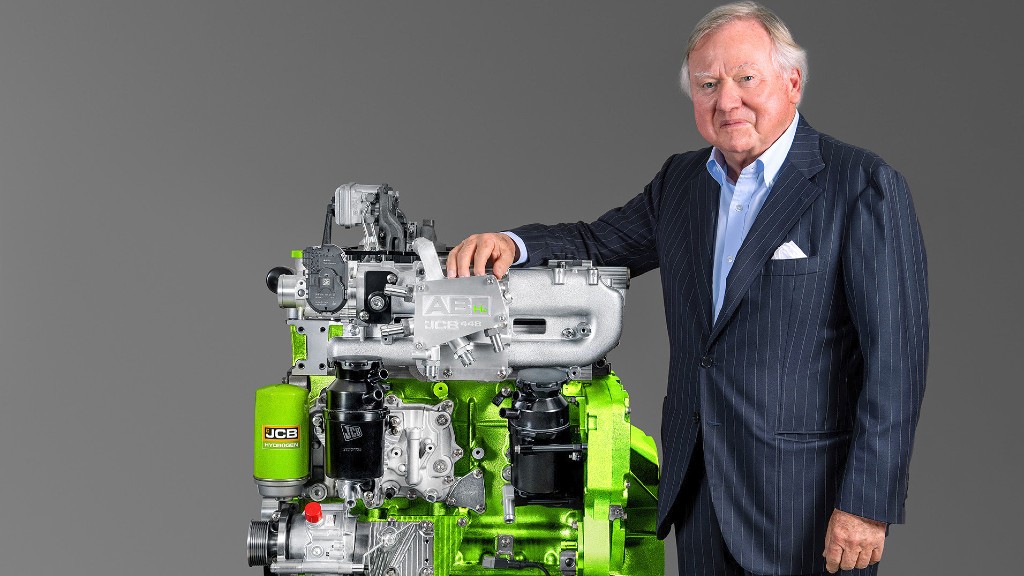 Lord Bamford stands with his arm on a hydrogen combustion engine