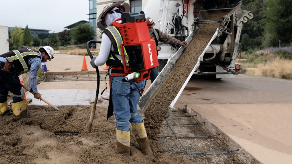 A worker wears a backpack concrete vibrator on a job site.