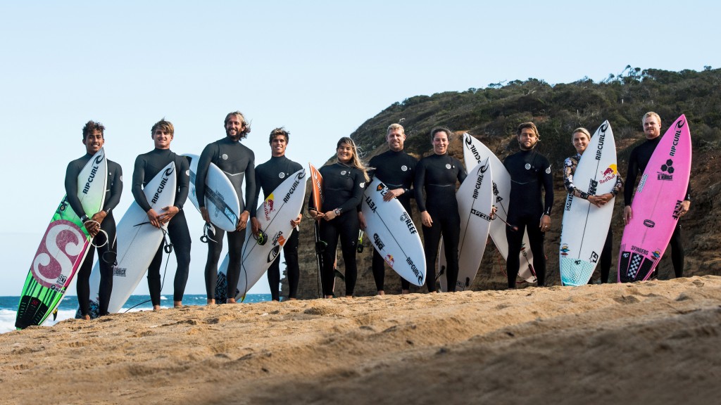 A large group of surfers stand on a beach