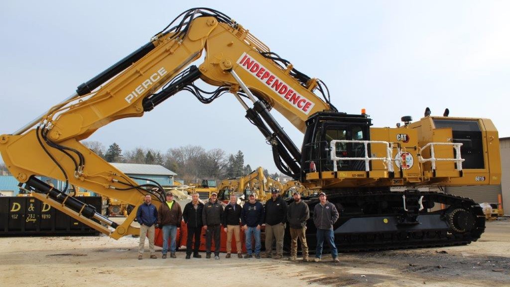 A group of people stand near a large demolition shovel