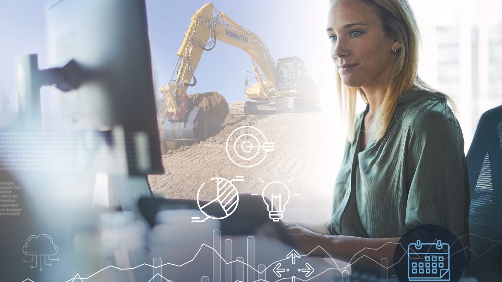 A woman uses a computer while an excavator operates in the distance