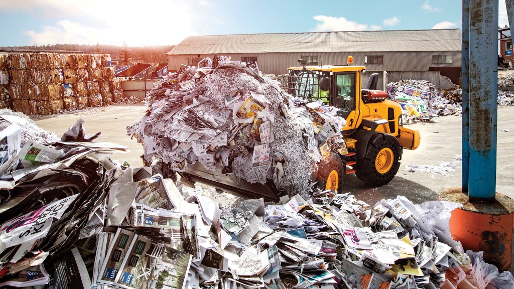 A scrap handler moves a bucket full of paper materials on a job site