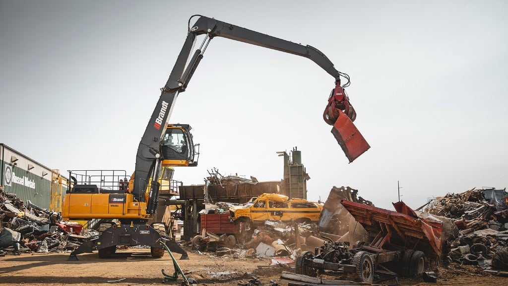 A material handler picks up a piece of scrap in a scrapyard