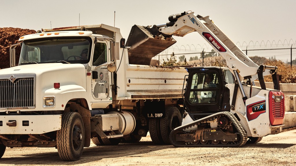 A compact track loader fills a truck with dirt