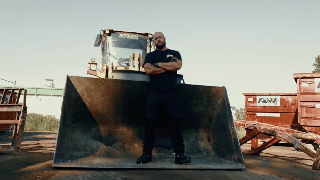 Byron Mikaloff stands in the bucket of a wheel loader