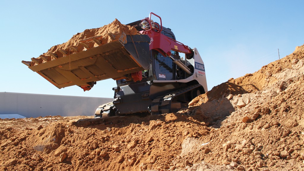 A compact track loader with a bucket full of dirt is parked near a ridge