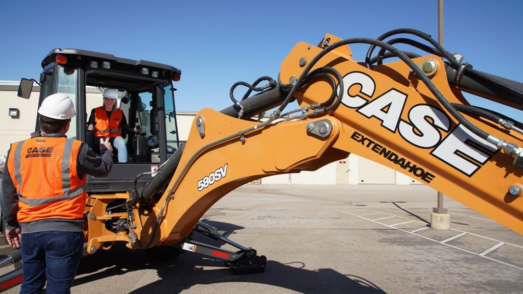 A young operator operates a backhoe loader in a parking lot