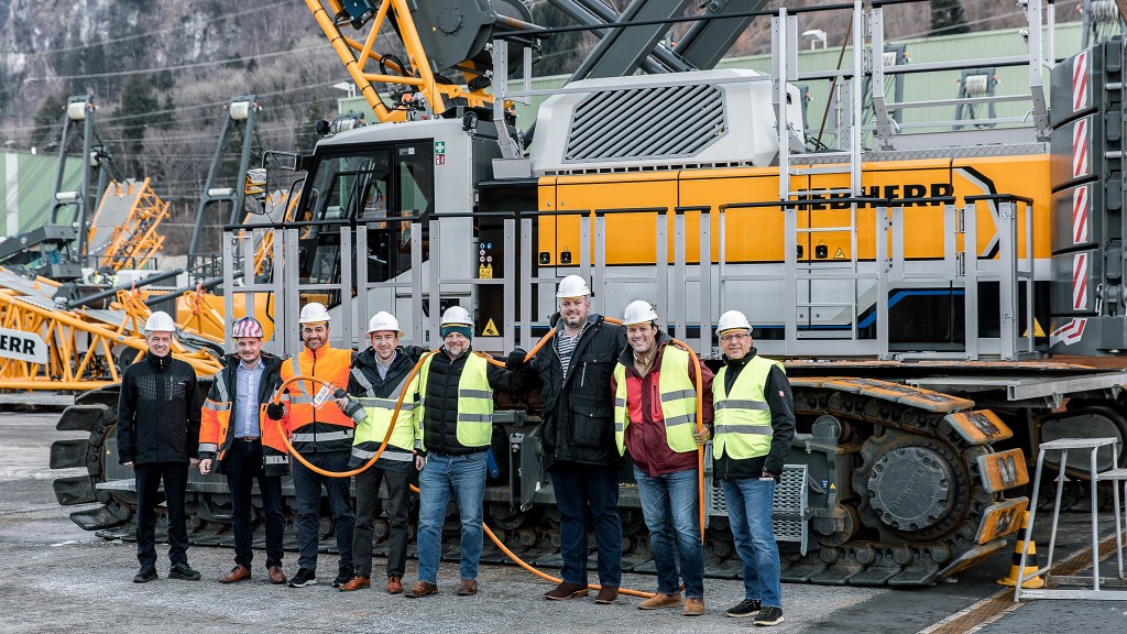 A group of people stand near a crawler crane