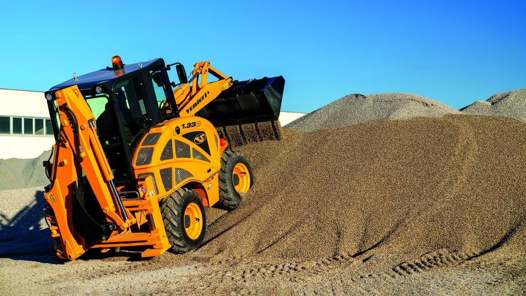 A compact backhoe loader pushing gravel up a hill.