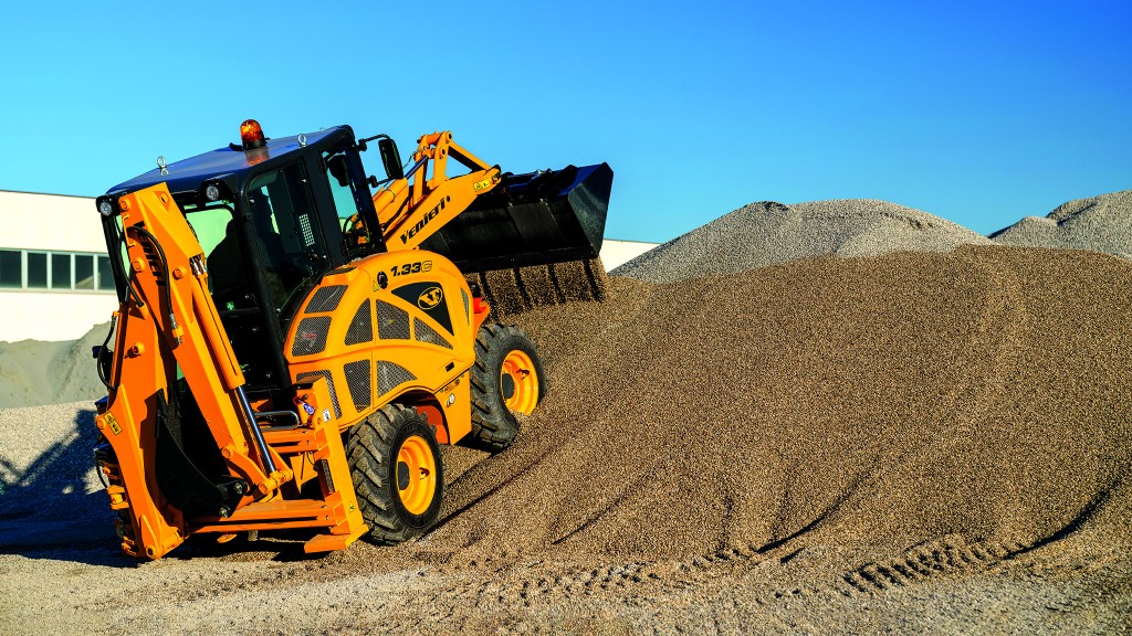 A compact backhoe loader pushing gravel up a hill.