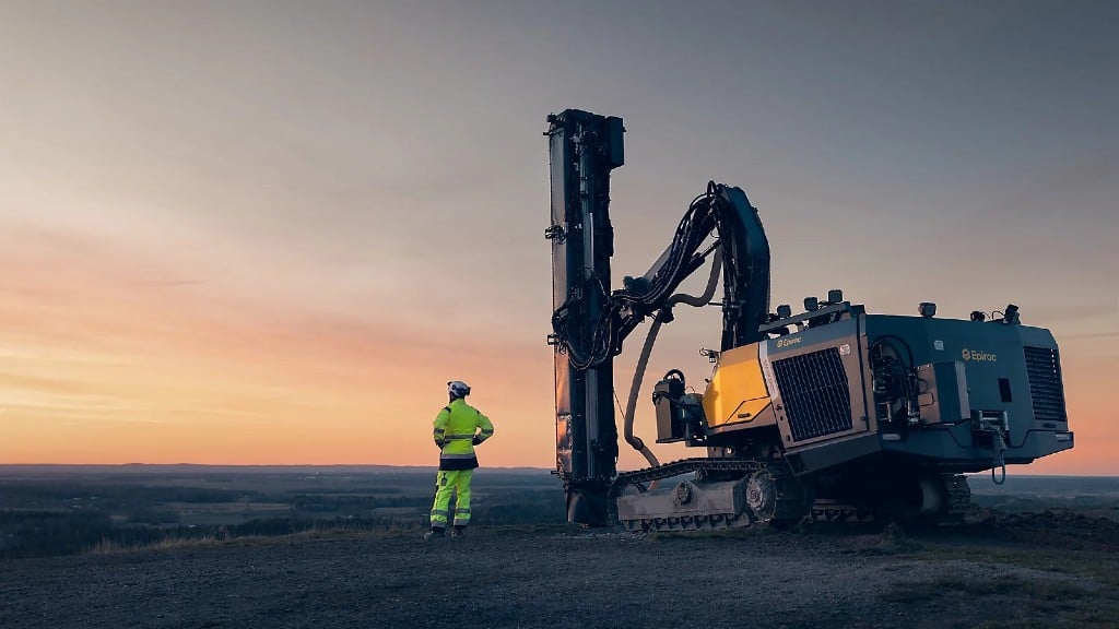 An operator stands near a drill rig with the sun setting in the distance