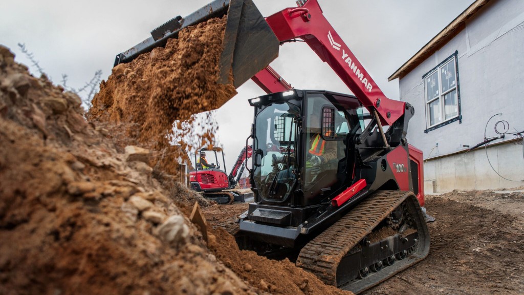 A compact track loader dumps a bucket of dirt on a job site
