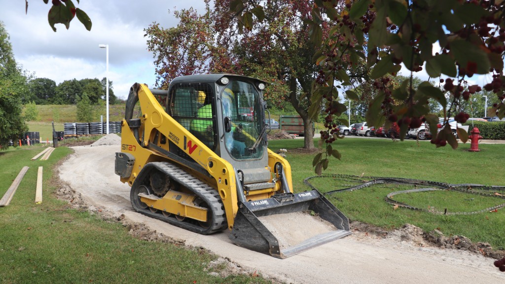 A compact track loader drives down a narrow path