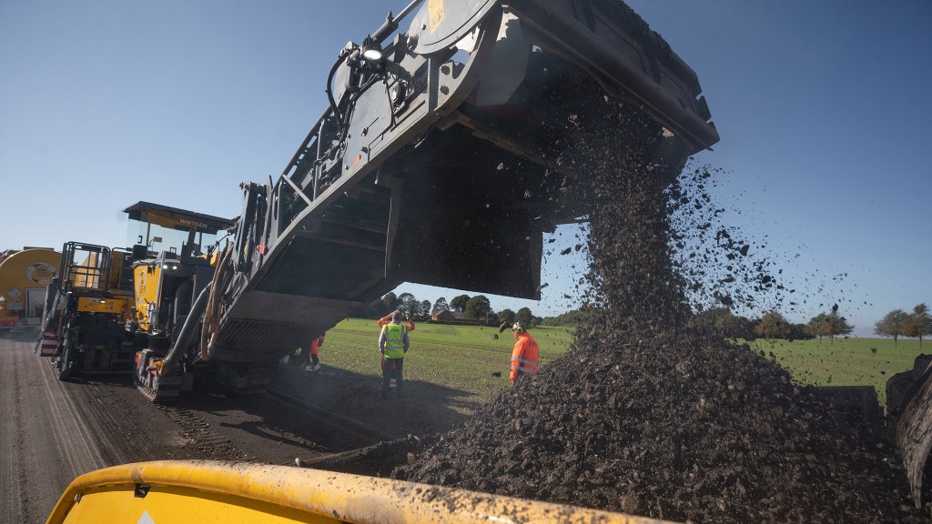 Pieces of asphalt fall from the conveyor of a cold recycling machine into a hopper.