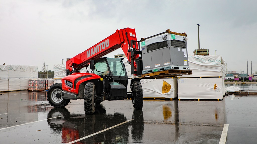 A telehandler hauling a load across a wet asphalt lot