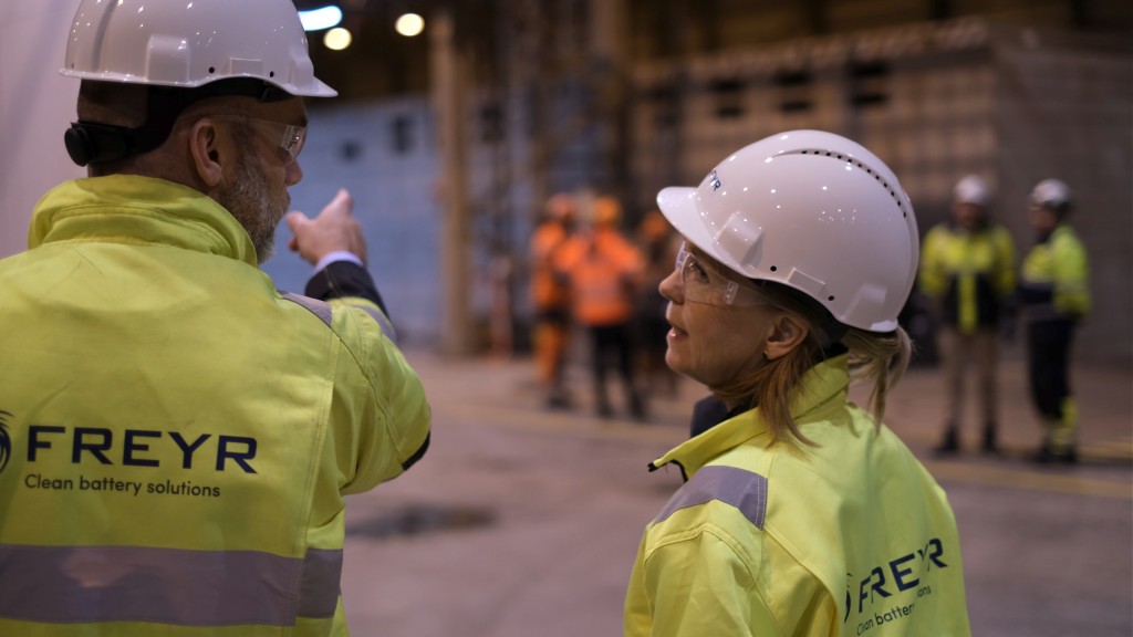 Two people in safety gear have a conversation inside a facility