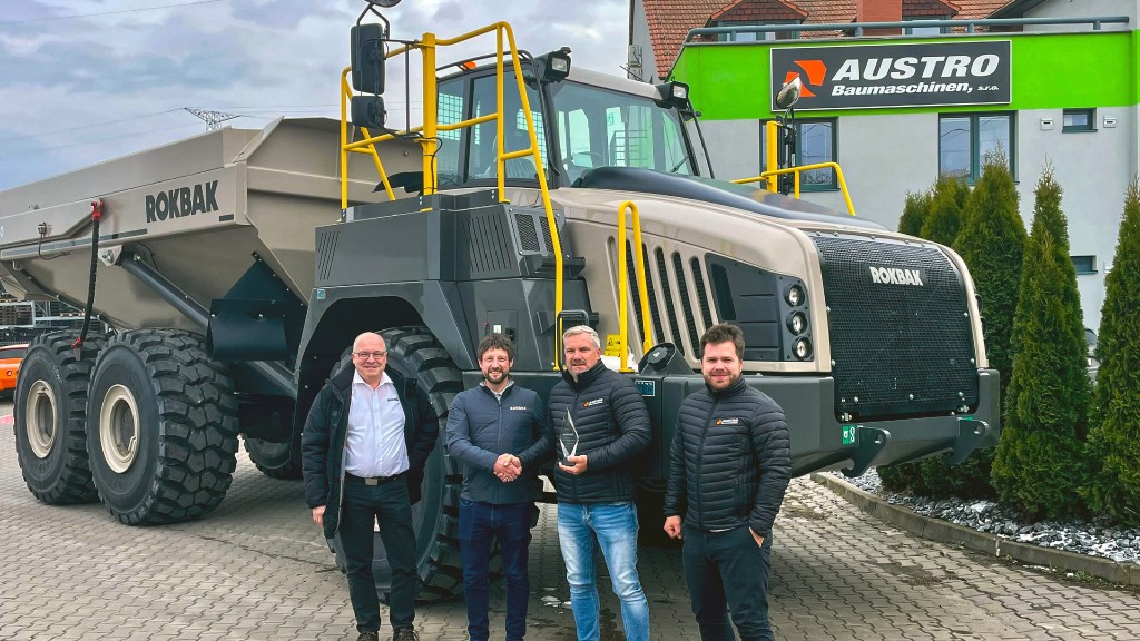 Four people pose for a photo in front of an articulated hauler