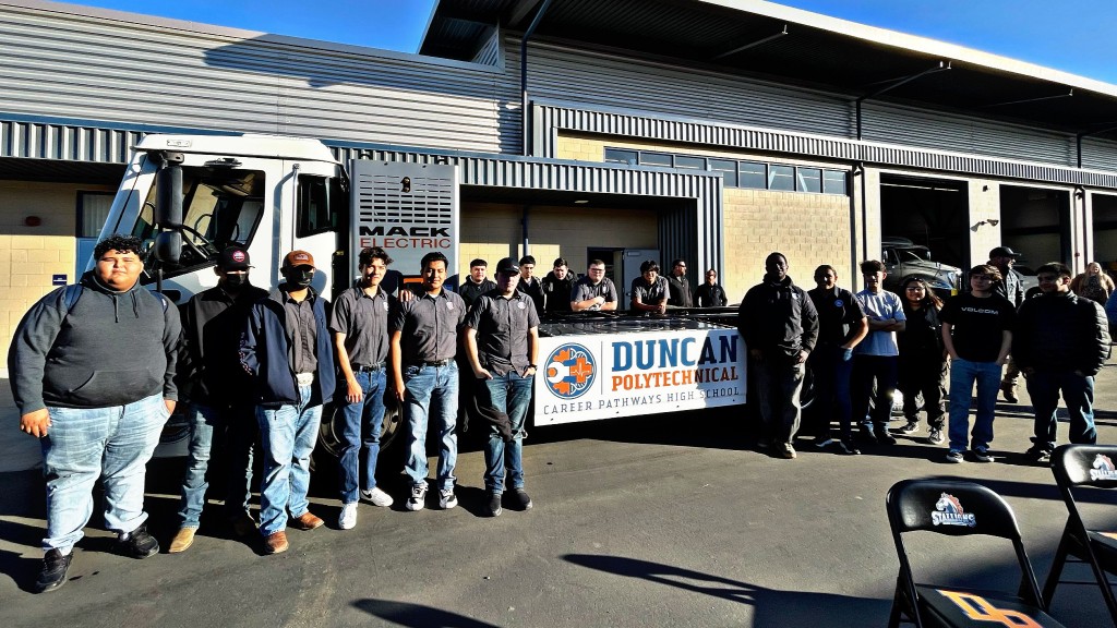 A group of people pose for a photo around an electric collection truck