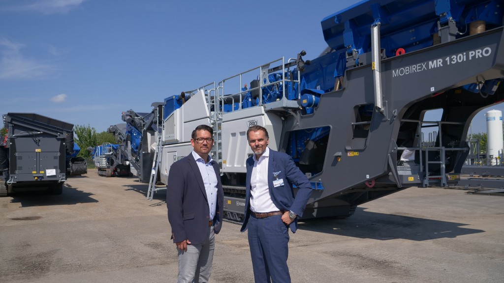 Two people pose for a photo near an impact crusher